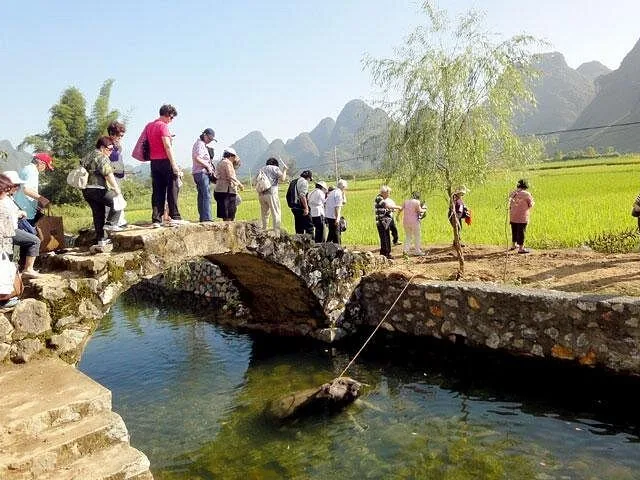 Group of tourists crossing a stone bridge over a small rural stream