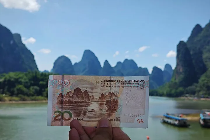 A 20 yuan banknote held up against the matching Li River scenery